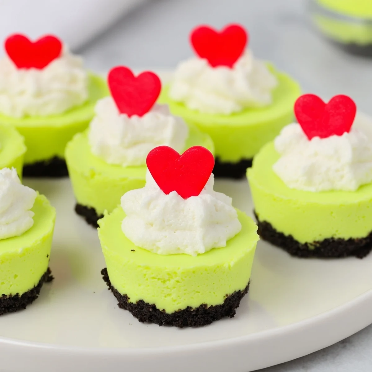 Bright green Grinch Mini Cheesecakes topped with fluffy whipped cream and festive sprinkles, ready to serve.