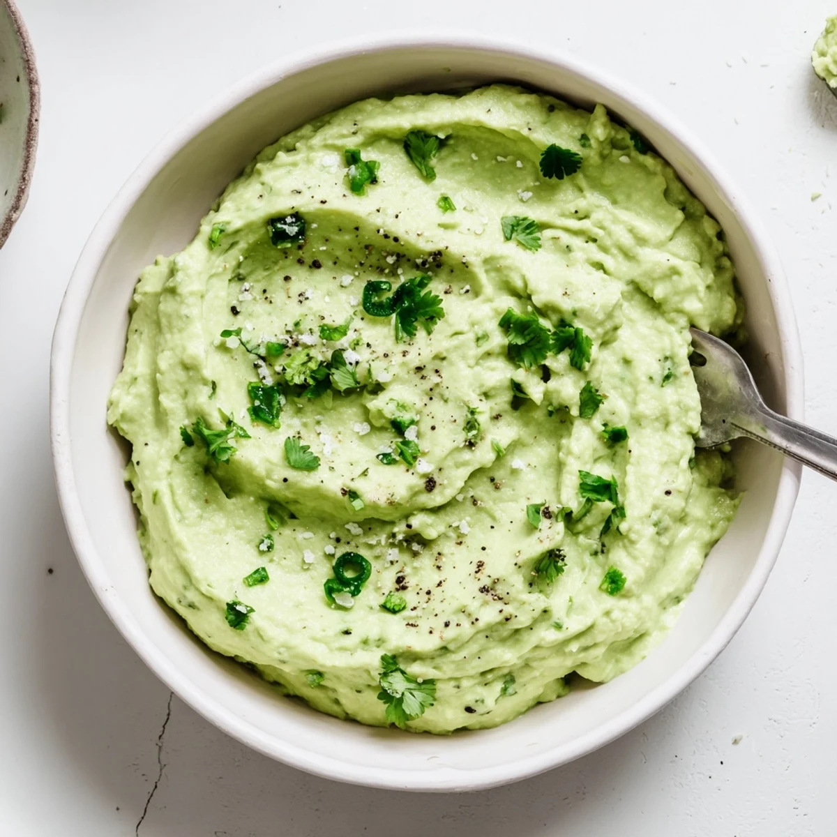 Creamy avocado lime dip in a rustic bowl, topped with cilantro and served with crunchy tortilla chips for dipping.