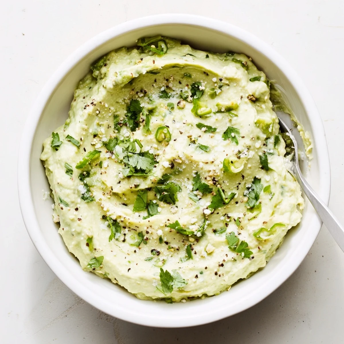 Vibrant green avocado dip with lime and cilantro, surrounded by fresh vegetable sticks for a healthy snack pairing.