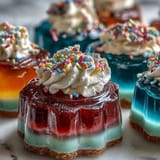 Colorful rainbow Jello cups featuring bright red, orange, yellow, green, blue, and purple layers, topped with whipped cream.