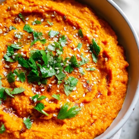 A close-up of creamy Carrot Ginger Dip in a rustic bowl, garnished with fresh cilantro and sesame seeds.