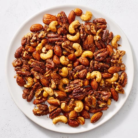 Golden roasted Spiced Nuts Mix glistening with honey and aromatic smoked paprika on a parchment-lined baking sheet.  
