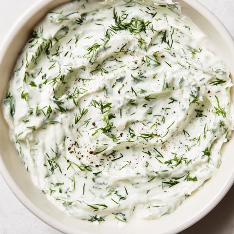 A bowl of creamy Greek Yogurt Herb Dip topped with fresh dill and chives, served with colorful vegetable sticks for dipping.  