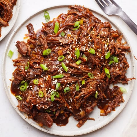 Savory Slow Cooker Honey Garlic Beef: Rich, dark sauce coats fork-tender shredded beef.