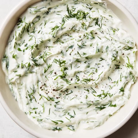 A bowl of creamy Greek Yogurt Herb Dip topped with fresh dill and chives, served with colorful vegetable sticks for dipping.  