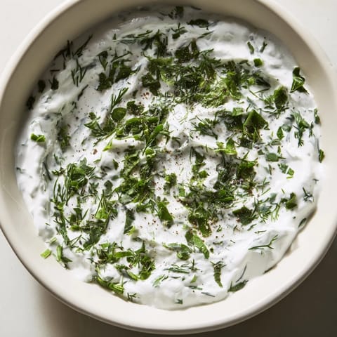 Thick, tangy Greek Yogurt Herb Dip in a rustic bowl, garnished with lemon zest and fresh herbs, alongside crispy pita chips.  