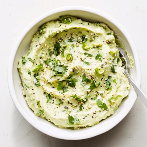 Vibrant green avocado dip with lime and cilantro, surrounded by fresh vegetable sticks for a healthy snack pairing.