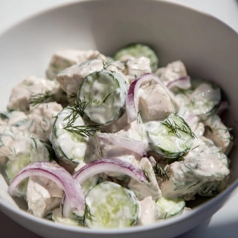 Overhead shot of Creamy Cucumber Chicken Salad served on a rustic wooden table, featuring vibrant cucumber ribbons, diced chicken, and a sprinkle of dill for a refreshing summer lunch.