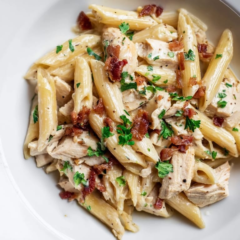 Sizzling bacon, tender chicken, and penne pasta coated in a luscious garlic-Parmesan cream sauce for an Italian-American family meal.