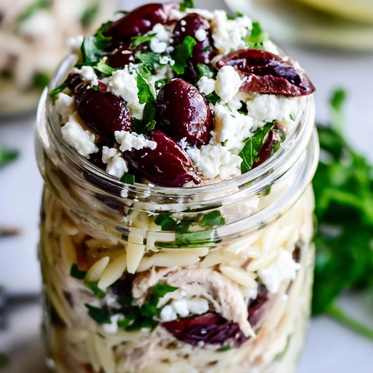 Close-up side shot of a Greek Pasta Chicken Salad Jar with Kalamata olives, cucumber, and red onion in olive oil dressing.
