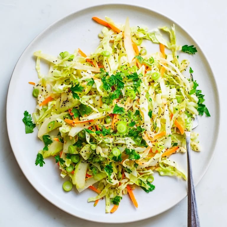 Freshly tossed Green Cabbage and Apple Slaw served in a white bowl, featuring shredded carrots and green onions for a colorful, crunchy side dish.