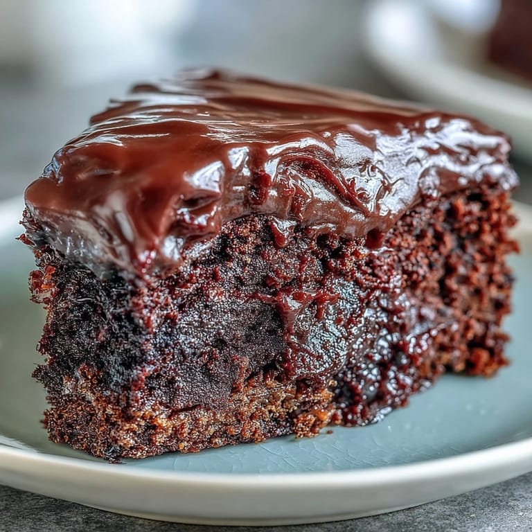A fork takes a bite of Easy Chocolate Fudge Cake, showing velvety chocolate icing and rich, squidgy texture inside.