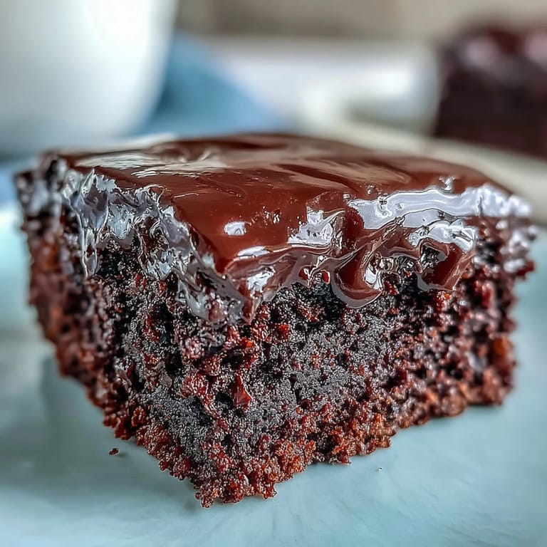 Dust of cocoa powder lightly covers the top of the Easy Chocolate Fudge Cake near a fresh cup of coffee.