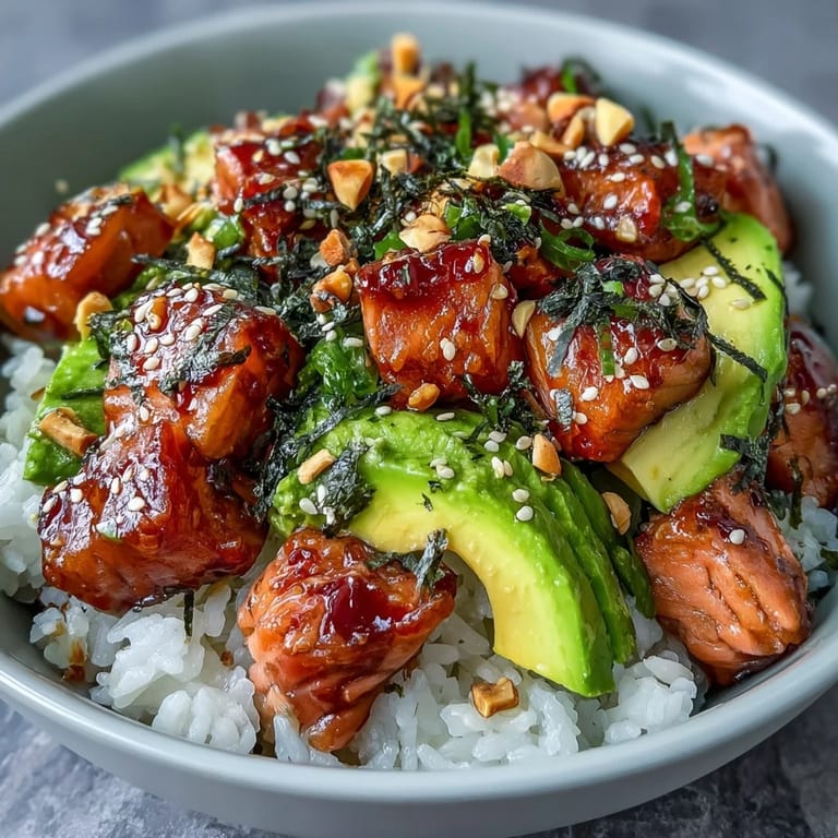 Colorful rice bowl featuring flaky salmon, buttery avocado, spicy chili oil drizzle, wasabi paste, and crunchy peanuts for a satisfying fusion meal.