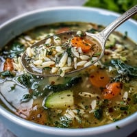 A warm bowl of Lemon Herb Soup topped with fresh parsley and dill, served next to lemon slices and crusty bread.